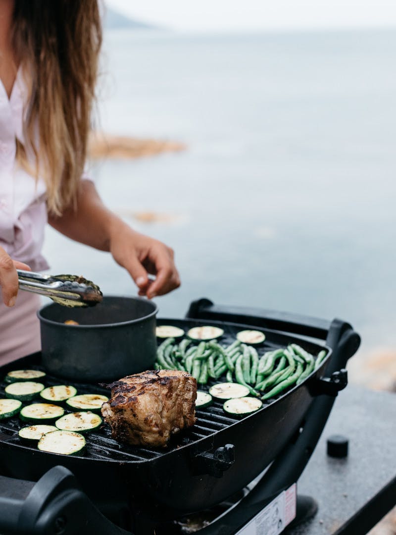Close up of Sarah Glover grilling food outside, with a pan on the grill.