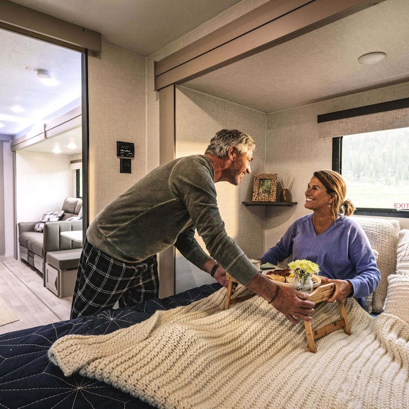 A couple having breakfast in bed inside a KZ RV.