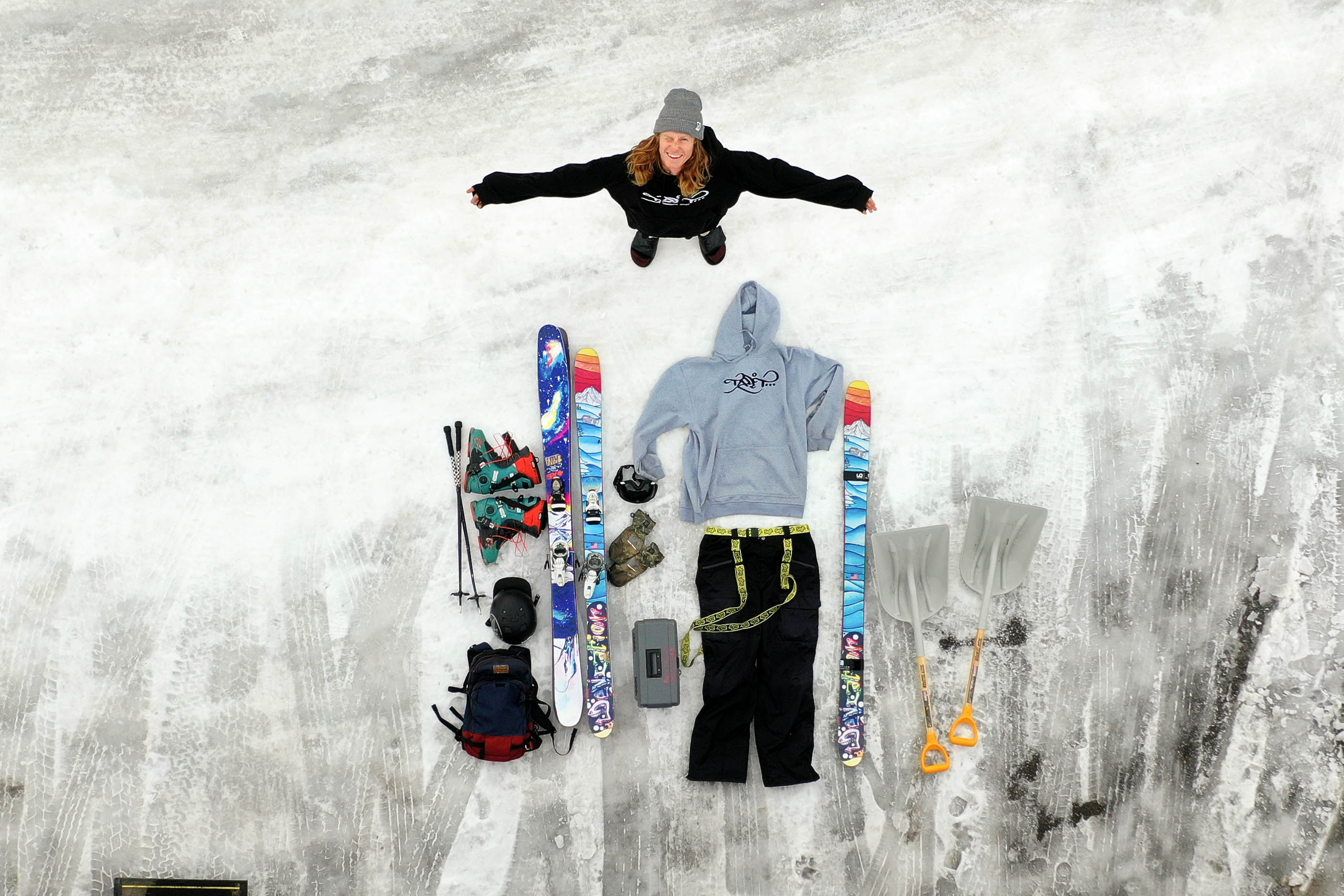 Ryan standing in an overhead shot of his ski gear laid out on the ground. 