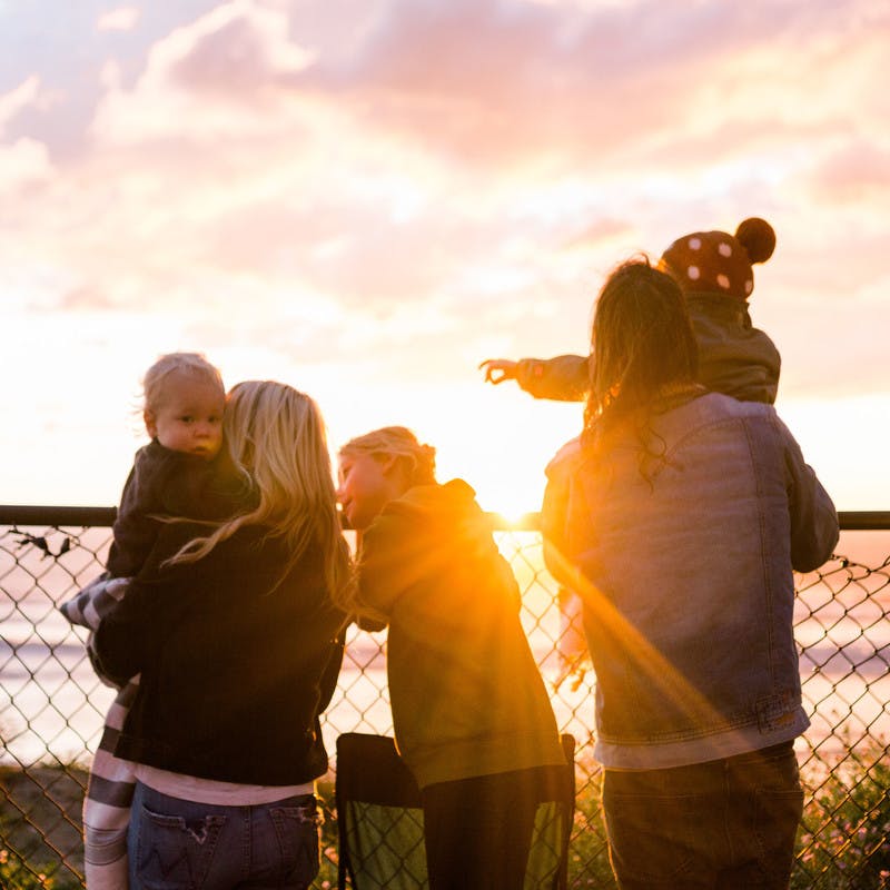 The Thrane family watching the sun set by a fence, with the beach and ocean in the background