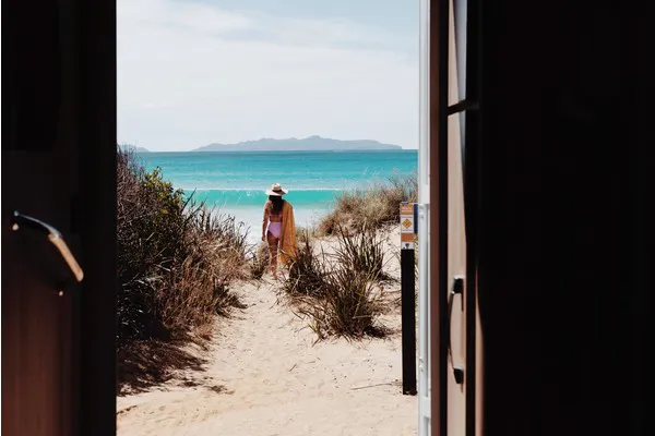 A view from the inside of an RV looking out the doorway to Kelvedon Beach, in Tasmania, Australia. With Sarah Glover in the background looking out to the ocean.