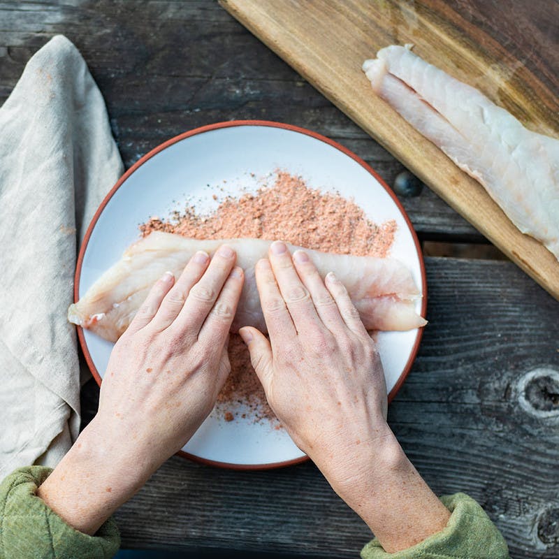 Woman uses hands to cover the rockfish in the spice blend.