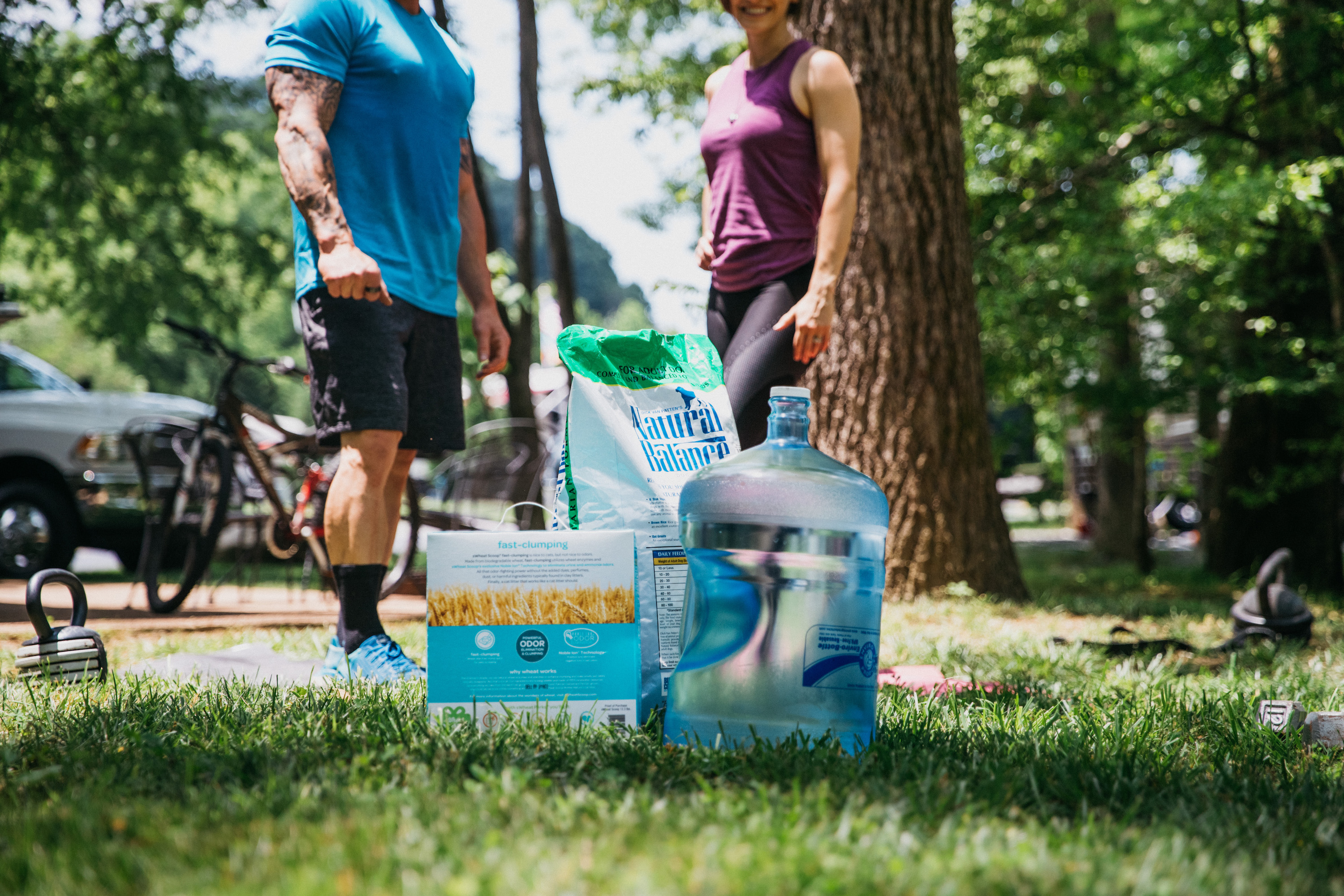 A 5-gallon water jug, a box of cat litter and a bag of dog food sitting in the grass, demonstrating what home items you can use as weights during a workout.