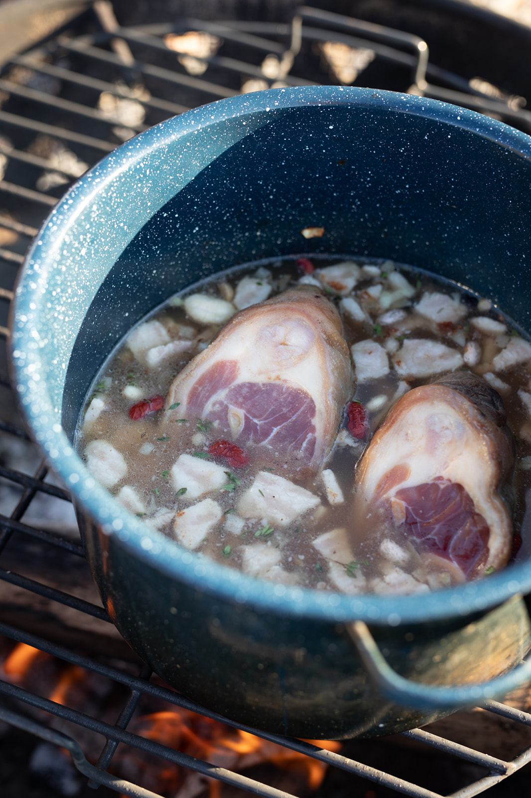 An enamel pot over a campfire with ham hocks and beans cooking inside.