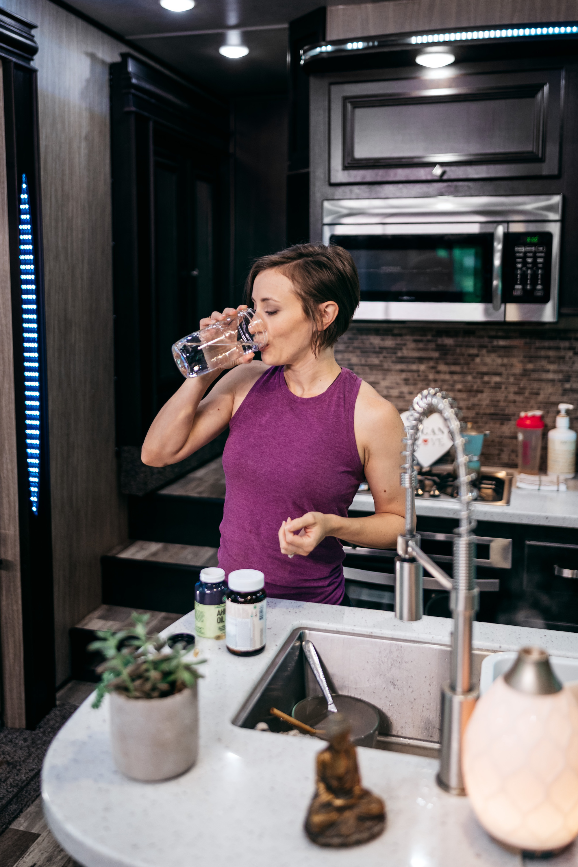 A woman in an RV kitchen taking vitamins with a glass of water. 