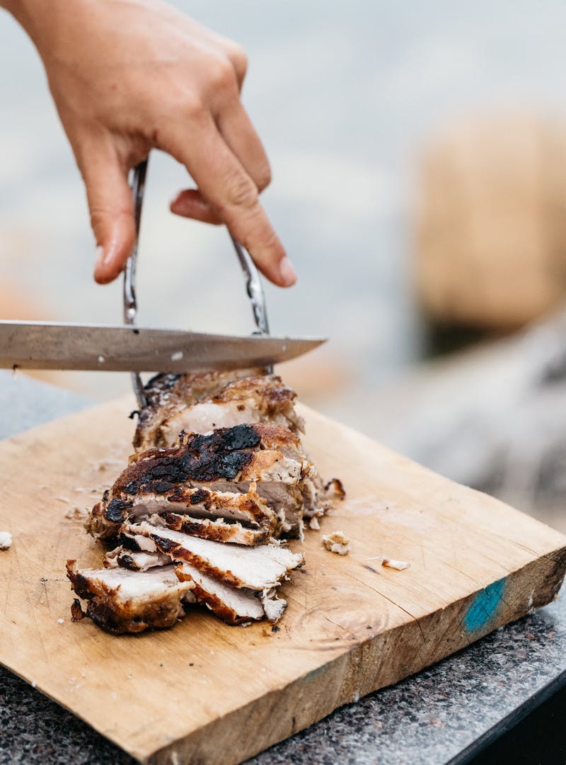 Close up of cutting pork with a knife on a cutting board.