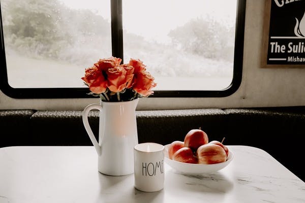A vase of roses, a bowl of crisp apples and a glowing candle that reads "home" on the kitchen table, in front of a foggy RV window.