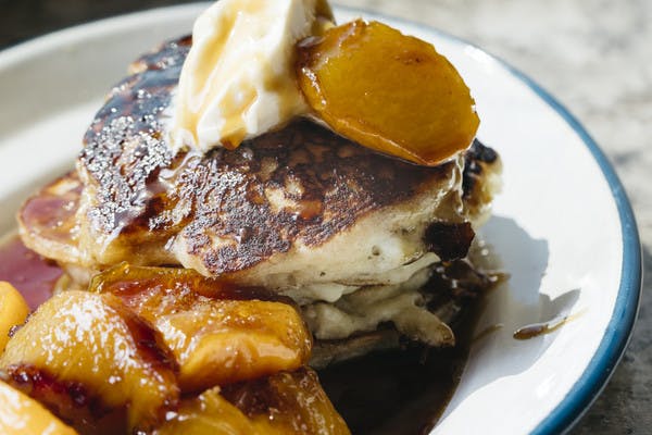 A plate of mini buttermilk pancakes with golden peaches and cream.