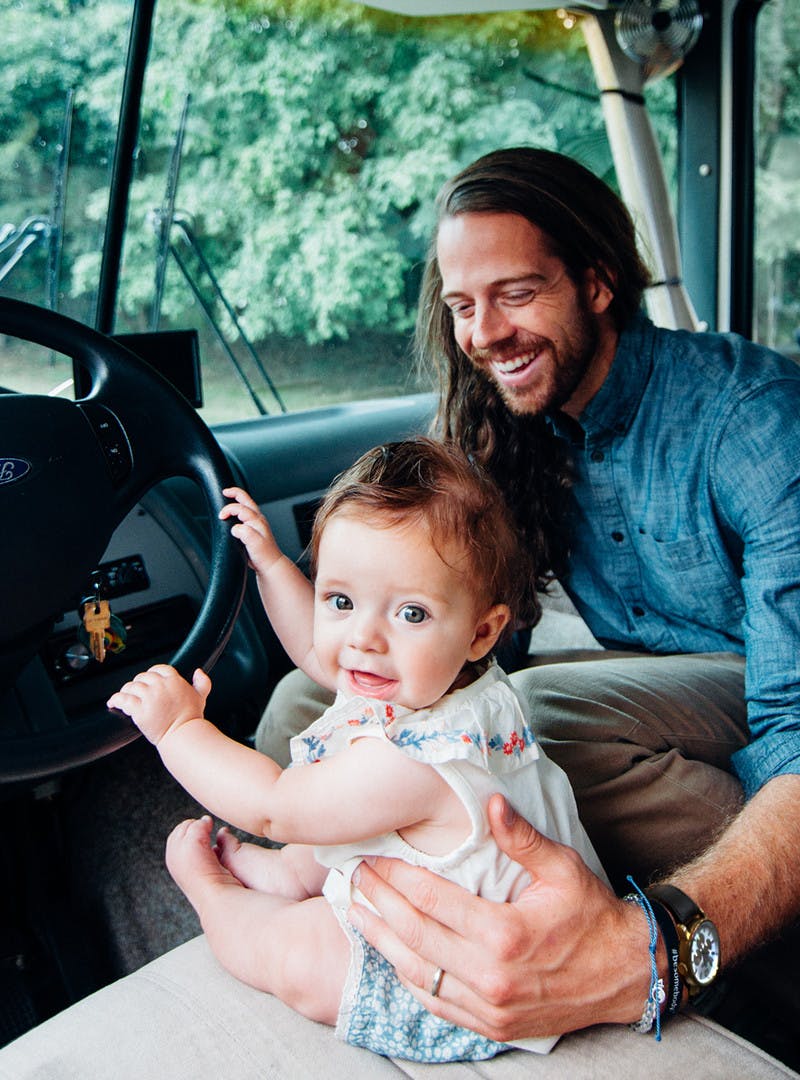 Bryce and Avalyn Jurgy inside the motorhome, baby trying to steer RV in driver's seat, while man holds and smiles from passenger seat.