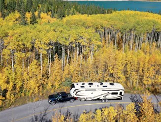 Fifth wheel towed down the road with lots of colorful fall trees