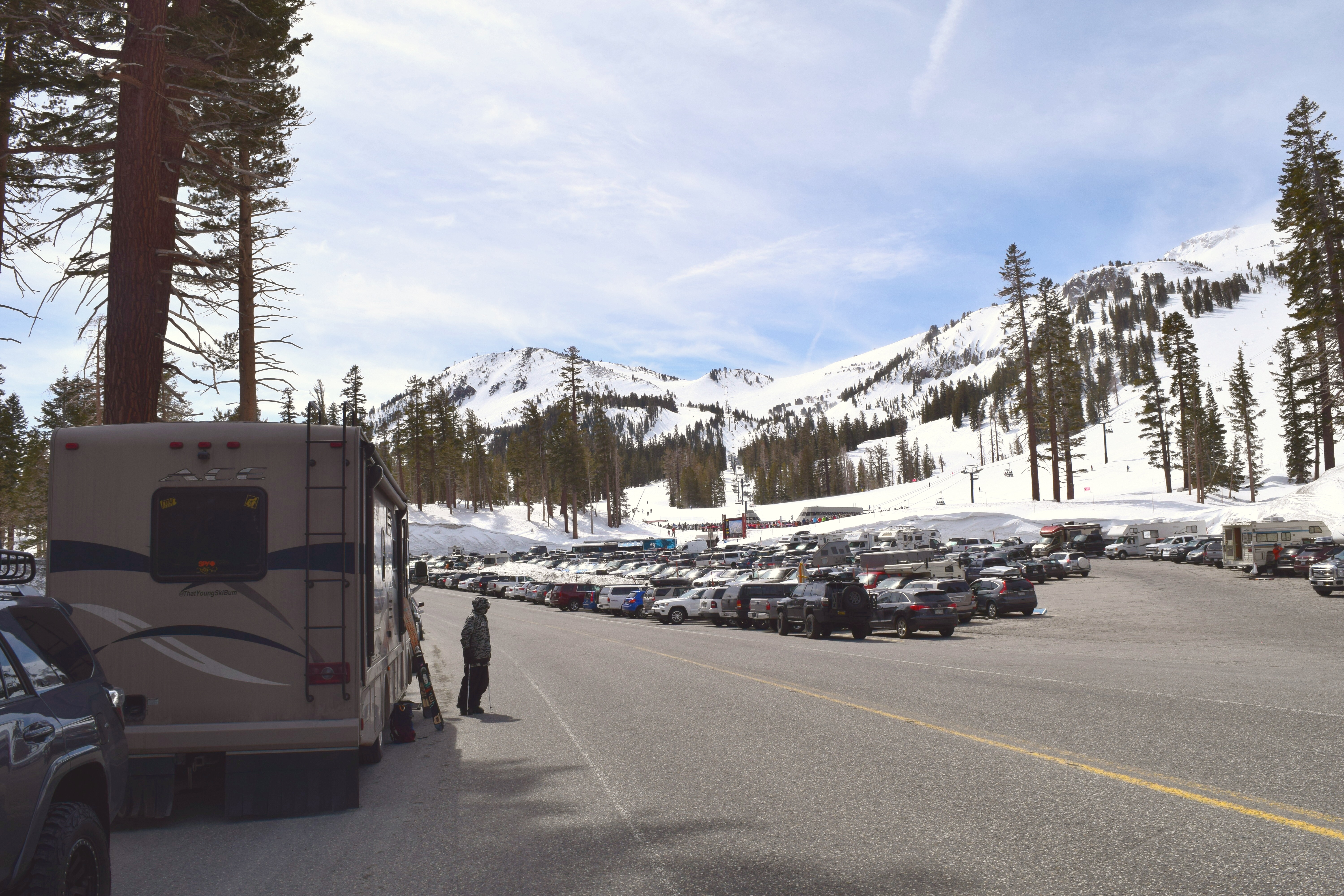 An RV parked on the side of the road next to a ski resort, with a mountain in the background. 