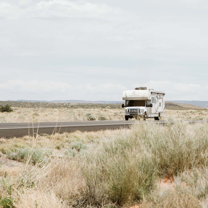 Class C motorhome drives along road, surrounding by plains with tall brown grass.
