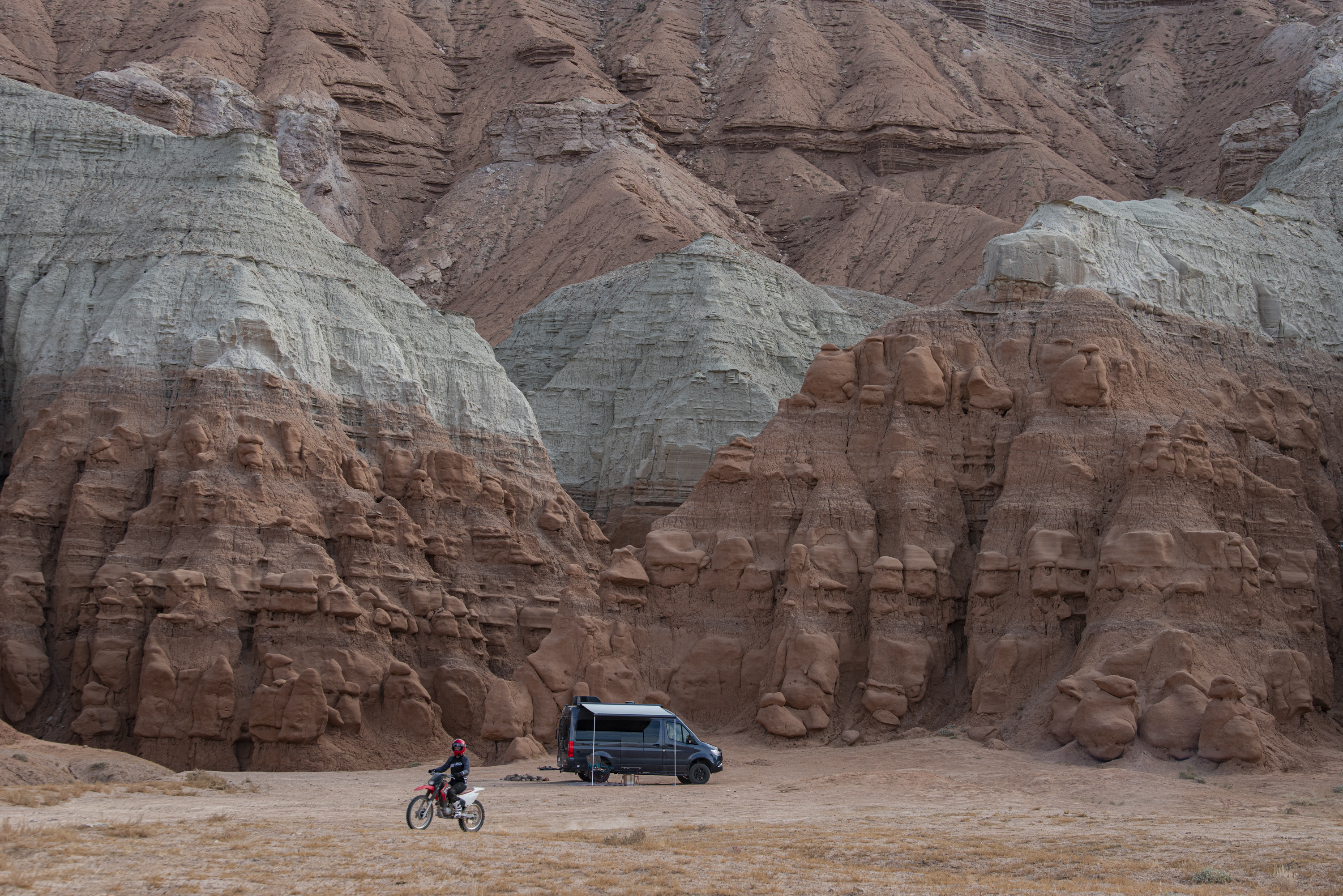 Kalen Thorien ridges a dirt bike in the desert with her TMC Sanctuary Class B RV parked.