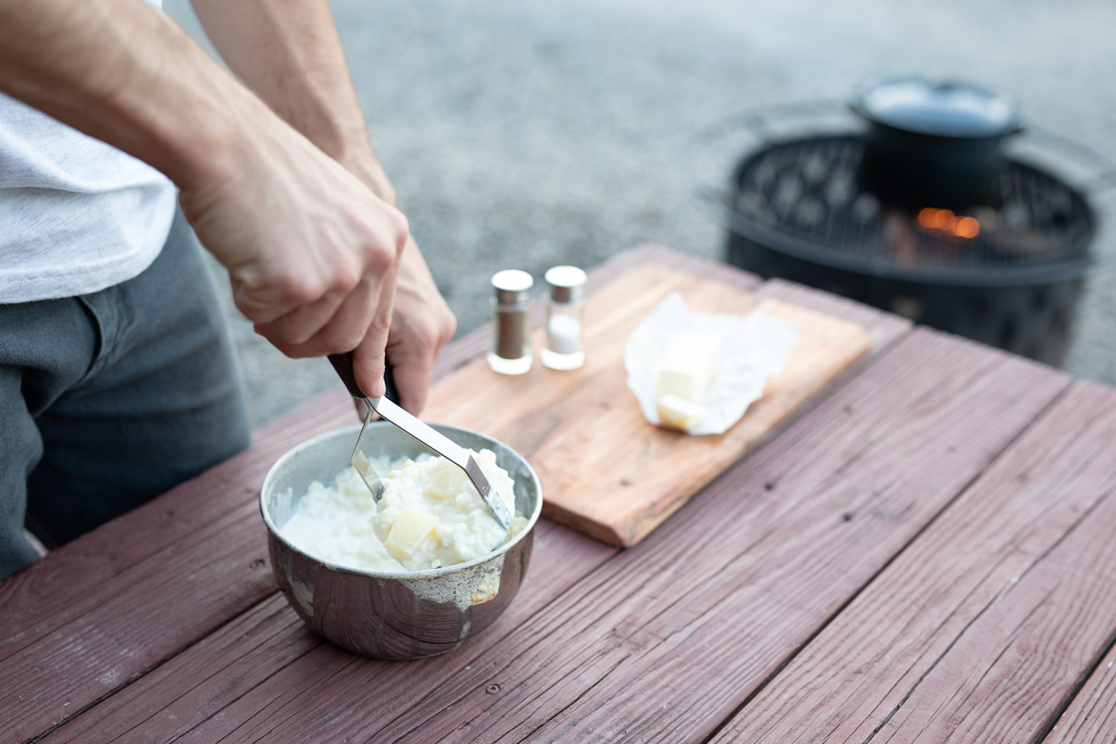 Mashing potatoes in a metal bowl with a potato masher. 