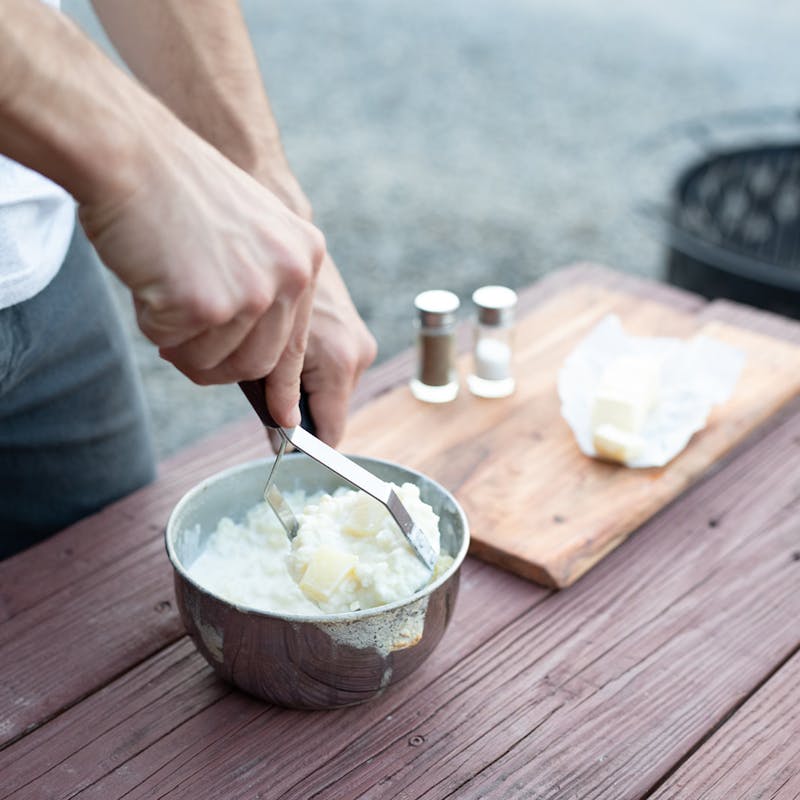 Mashing potatoes in a metal bowl with a potato masher.