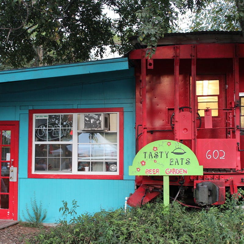 The Crum Box Gastgarden restaurant, a blue building with red train caboose and green beer garden sign, in Railroad Square Art Park in Tallahassee, Florida.