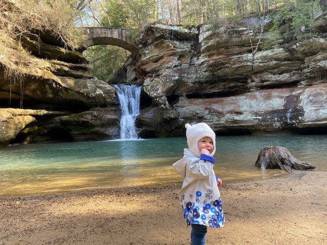 A small child captured in front of a natural waterfall. 