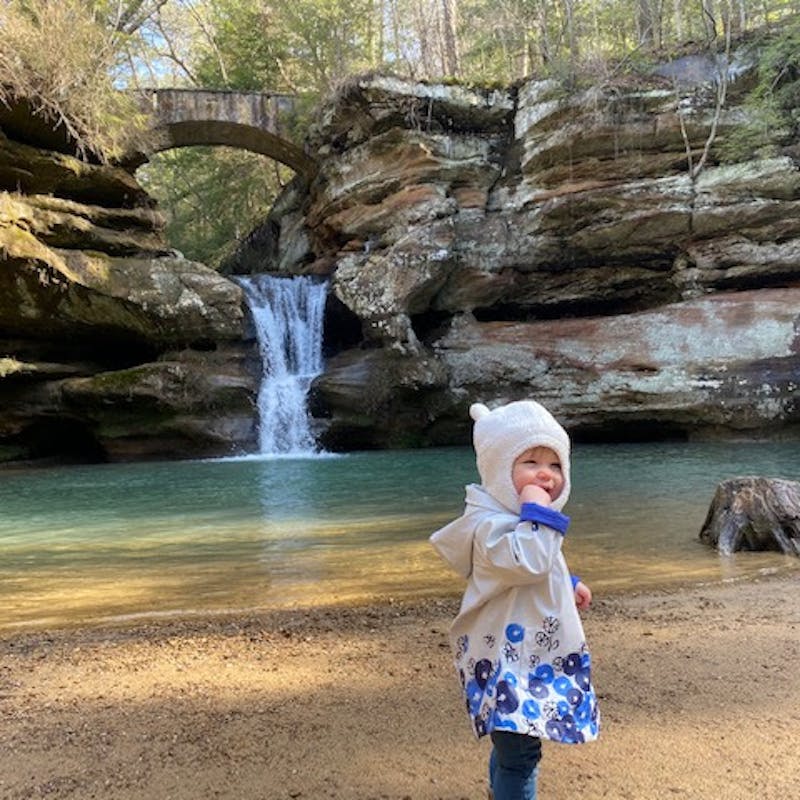 A small child captured in front of a natural waterfall.