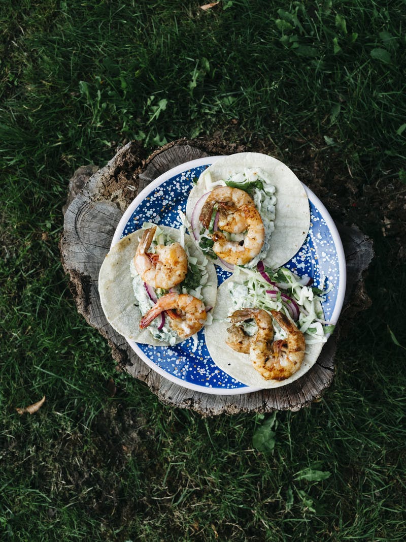 A plate of three assembled shrimp tacos, sitting on a tree stump outside.