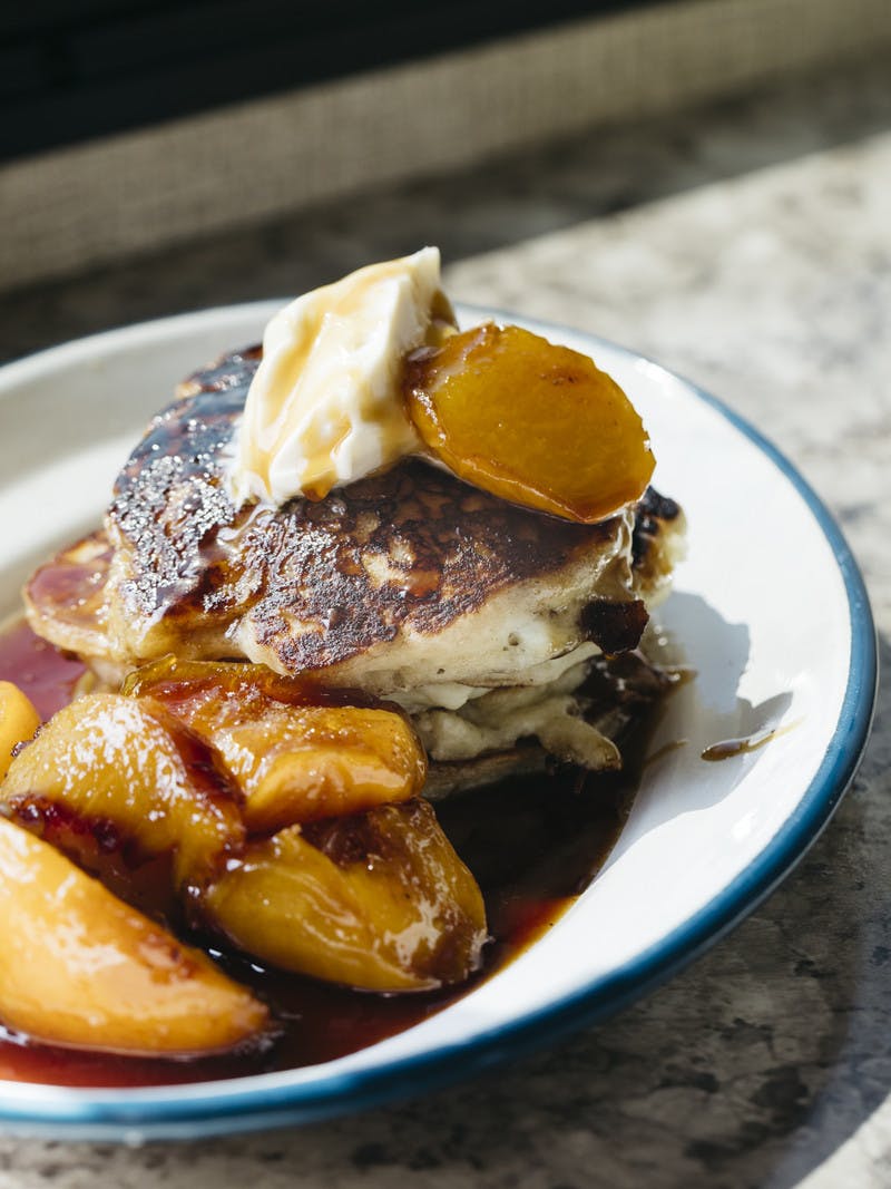 A plate of mini buttermilk pancakes with golden peaches and cream.