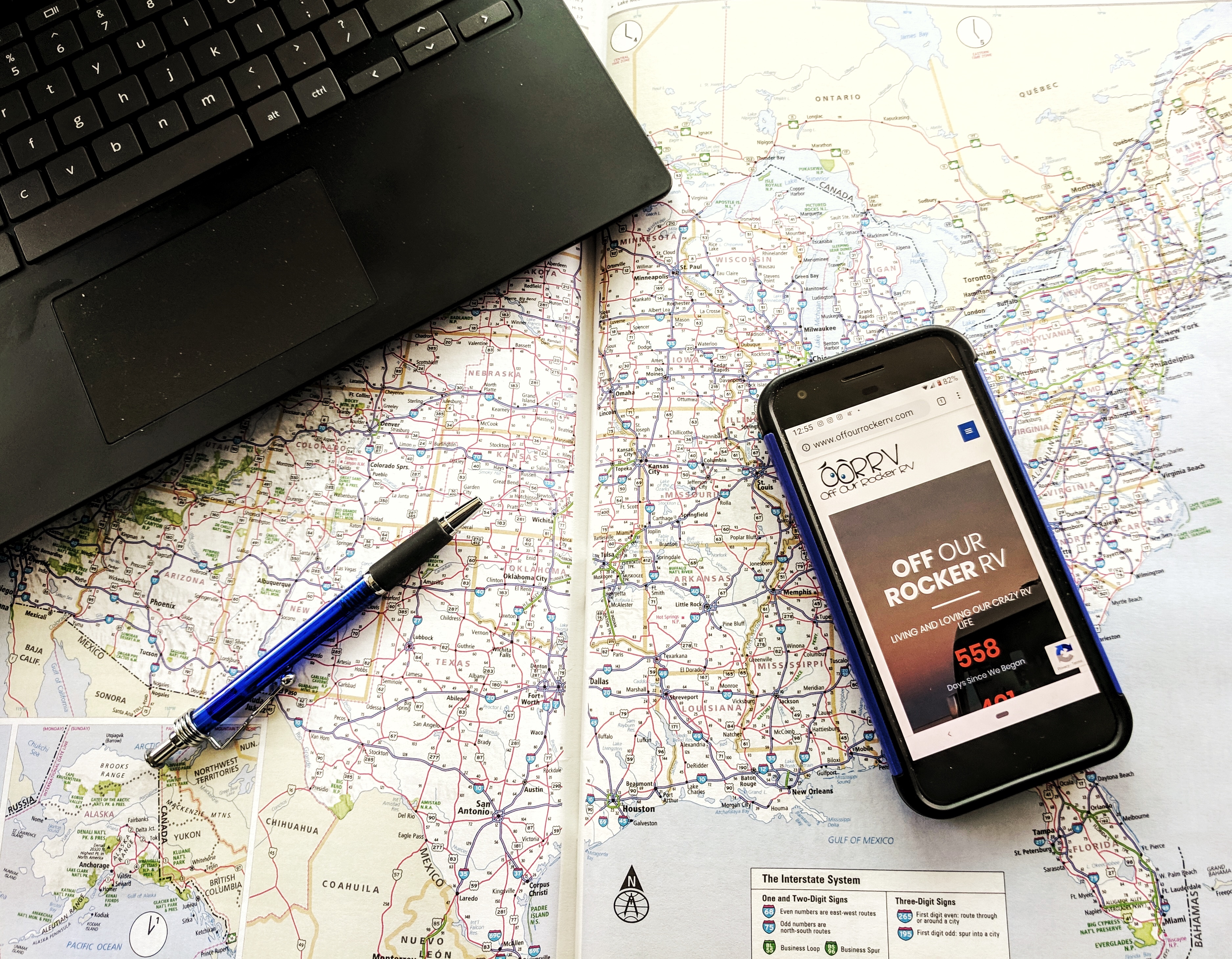 A phone and a laptop on top of a paper map of the United States. 