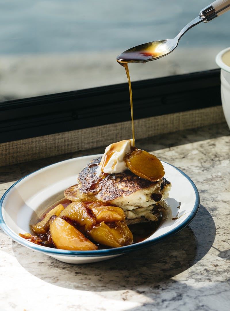 Plate of mini buttermilk pancakes with final touches of blueberries and peach liquid being added.