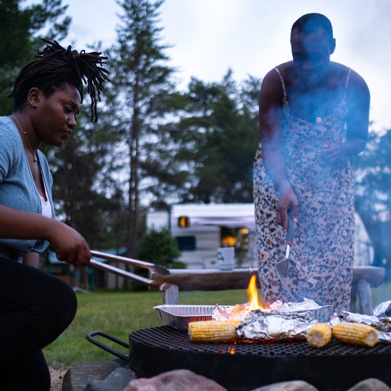 Chanel and Brittany Tate cooking over an open fire with a Jayco Travel Trailer RV in the background.