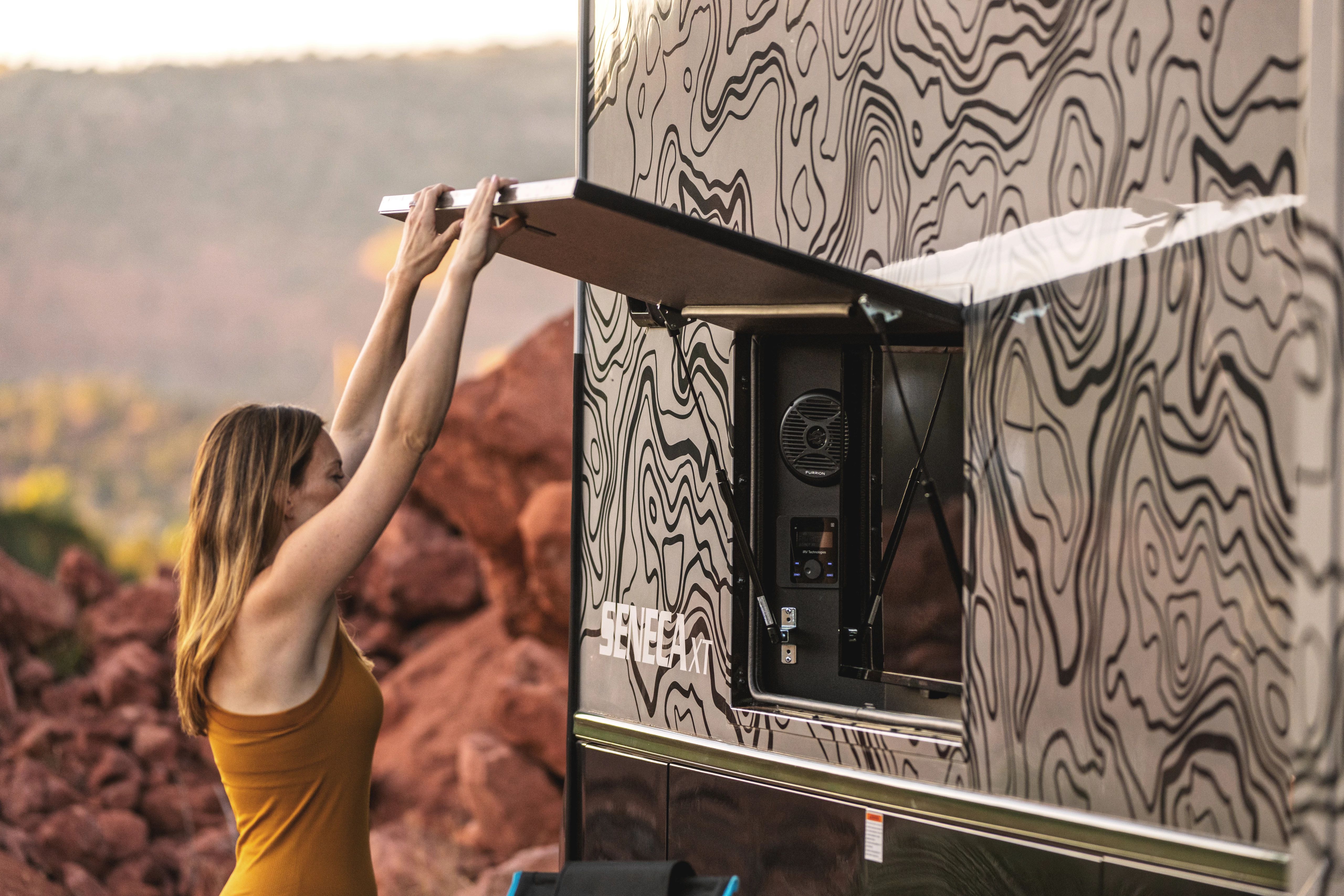A person closes the hatch on an exterior storage component within a Jayco Seneca Super C (Class C motorhome)