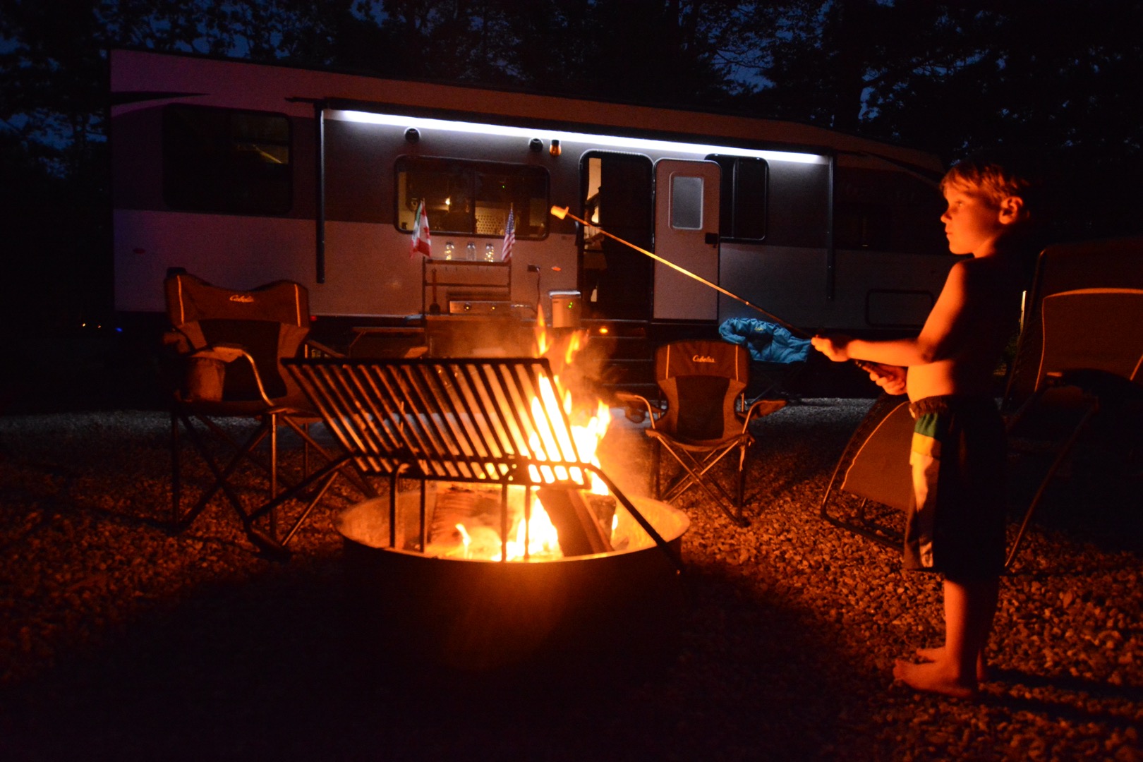 A little boy roasting a marshmallow over a campfire.