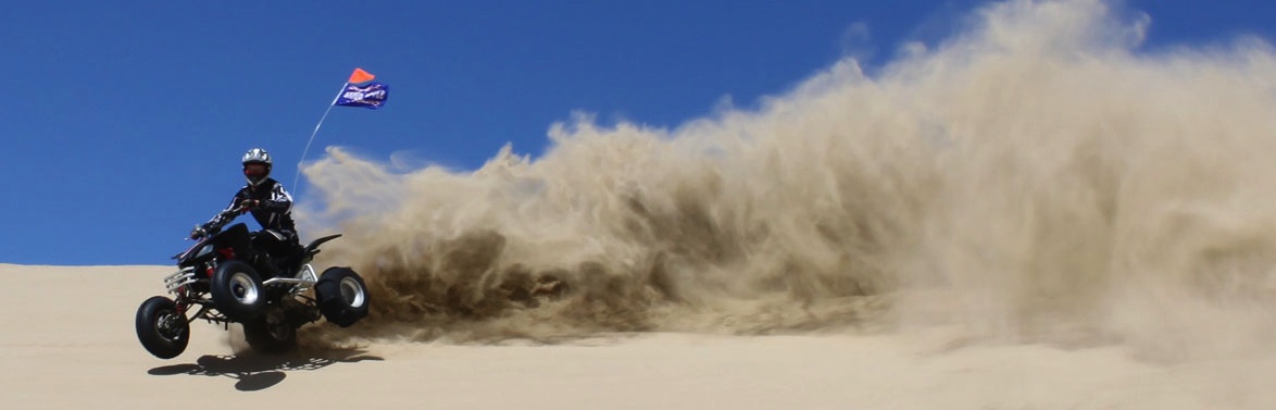 A quad bike rider throwing up sand at Oceano Dunes.