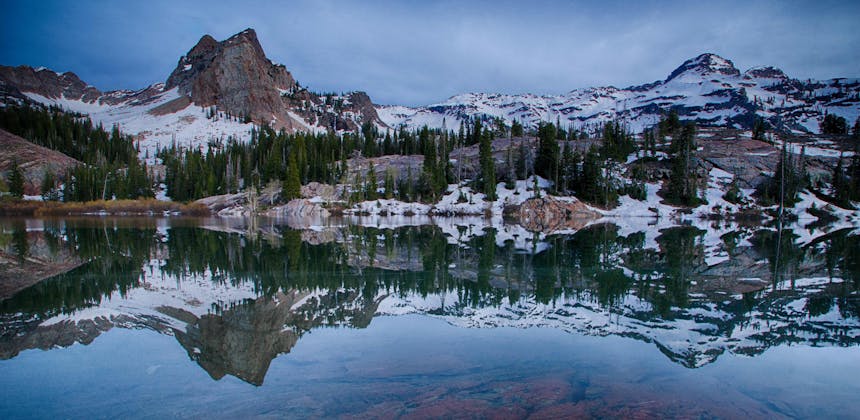 The reflection of snowy mountains and pine trees in Lake Blanche in Uinta-Wasatch-Cache National Forest.