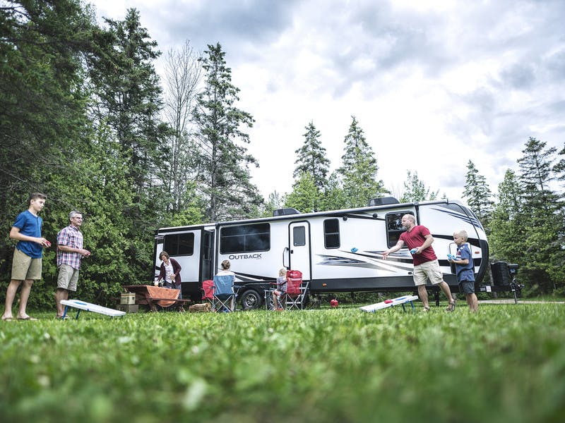 Family playing corn hole in front of travel trailer rv