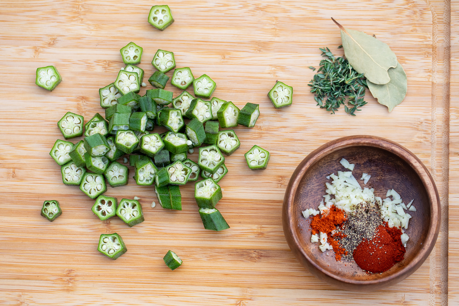 Chopped okra on a cutting board alongside a bowl of spices. 