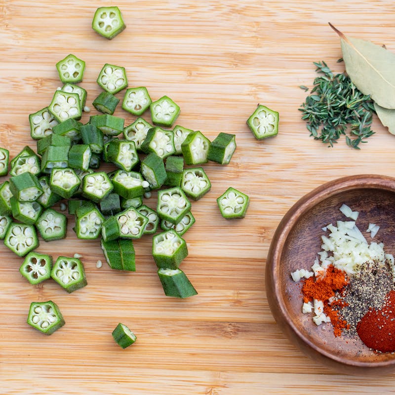 Chopped okra on a cutting board alongside a bowl of spices.