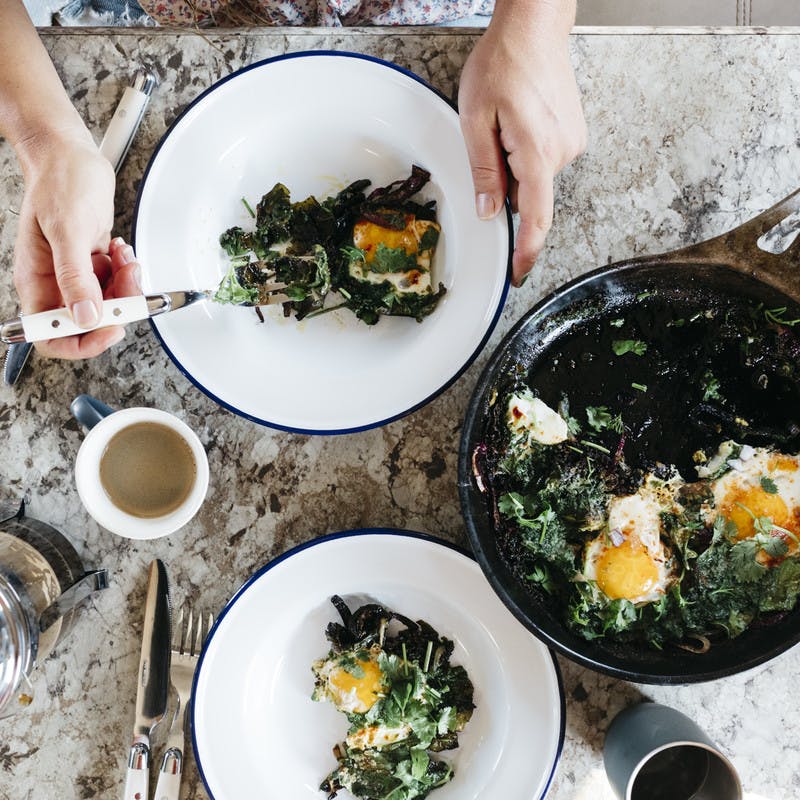 Overhead shot of swiss chard and pesto shakshuka over tabletop being eaten. 