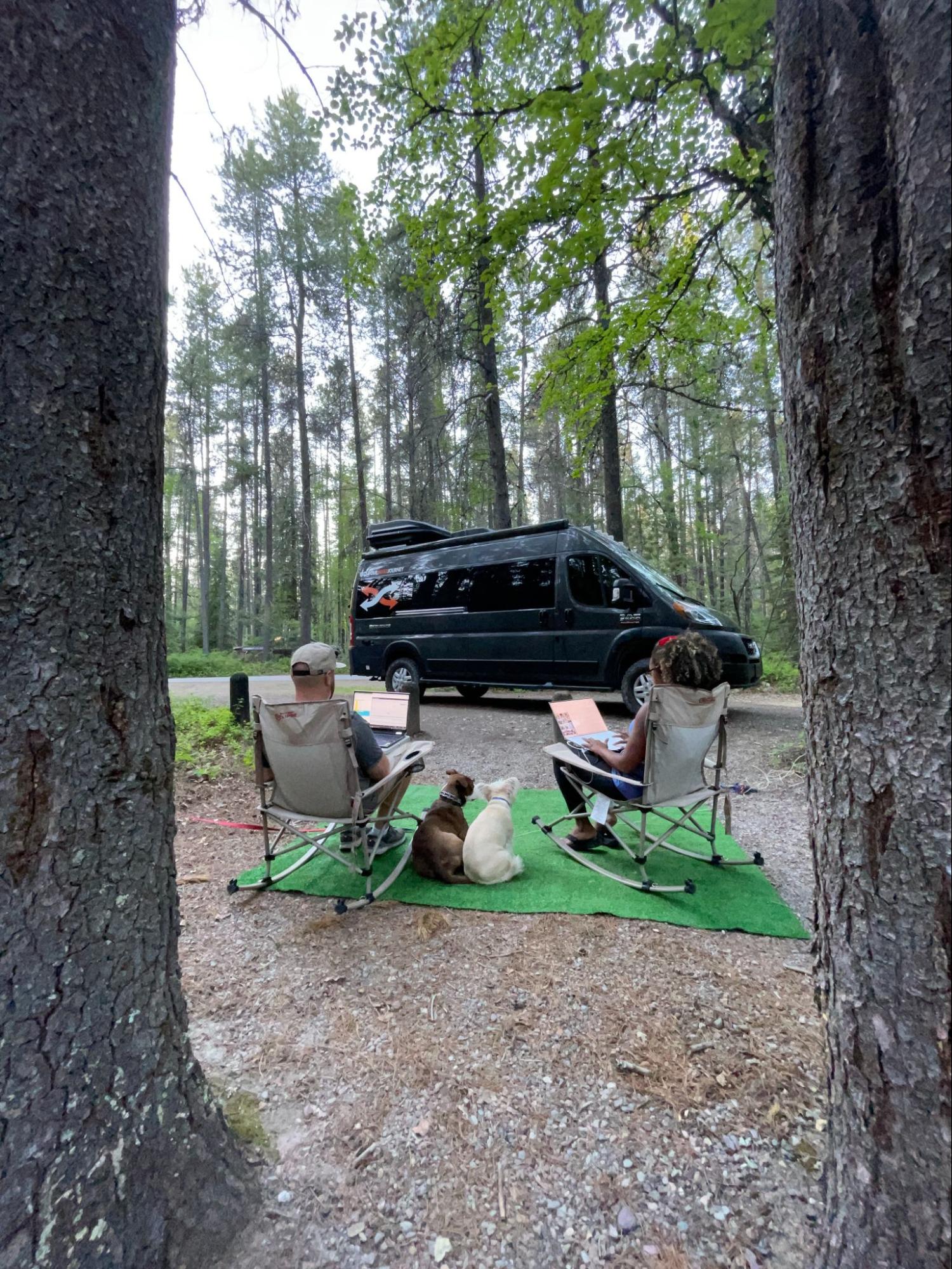Rocio and Gabe sit outside in rocking camp chairs in front of their Class B RV.