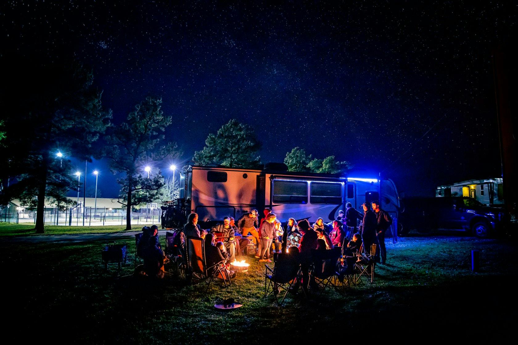 Josh and Cassie Bailey sitting around a campfire at night with lots of friends 