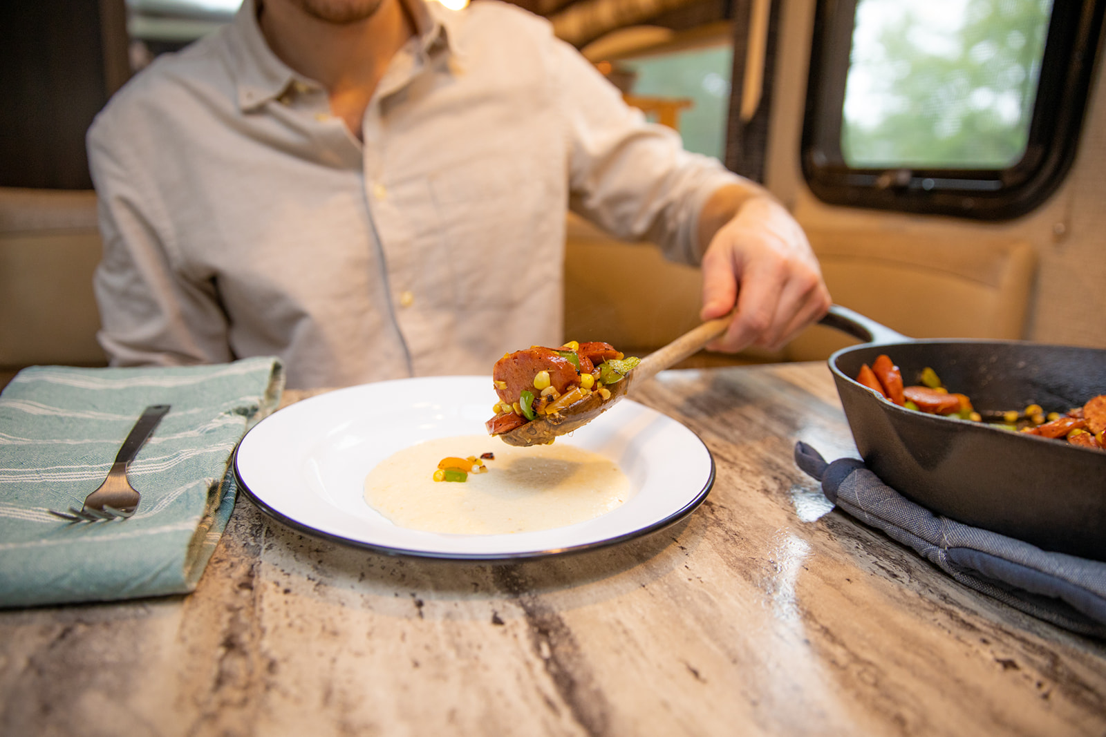 A man spooning veggies and sausage over a bowl of grits.
