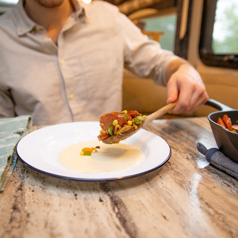 A man spooning veggies and sausage over a bowl of grits.