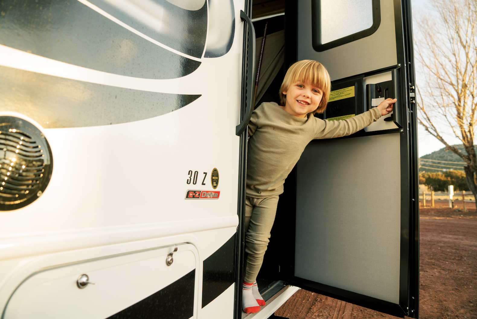 Little boy opens front door of Thor Class C motorhome and smiles out at the camera