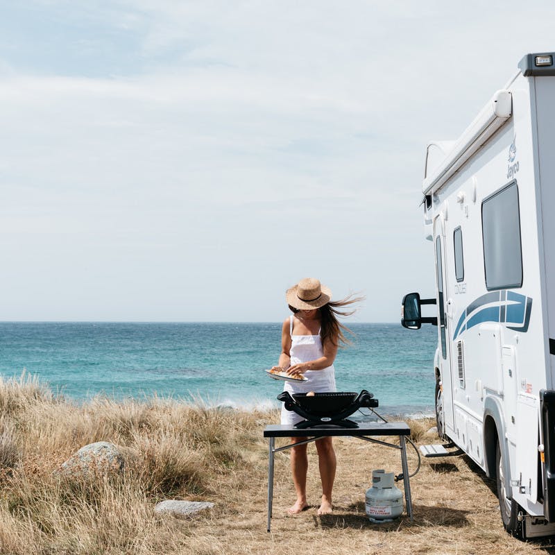 Sarah Glover cooking on a table by the ocean next to Class C motorhome.