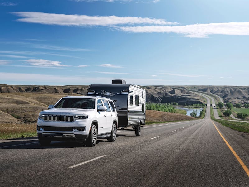 A lightweight travel trailer driving down the road being towed by an SUV