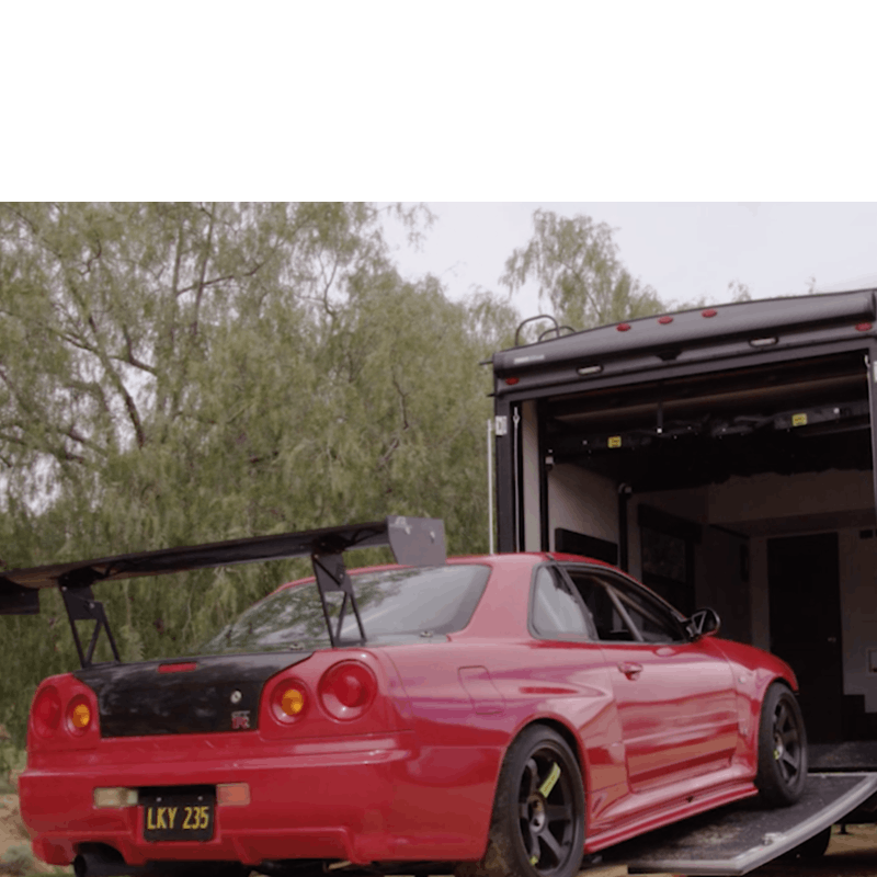 A red racecar being loaded into a Highlander Toy Hauler RV.