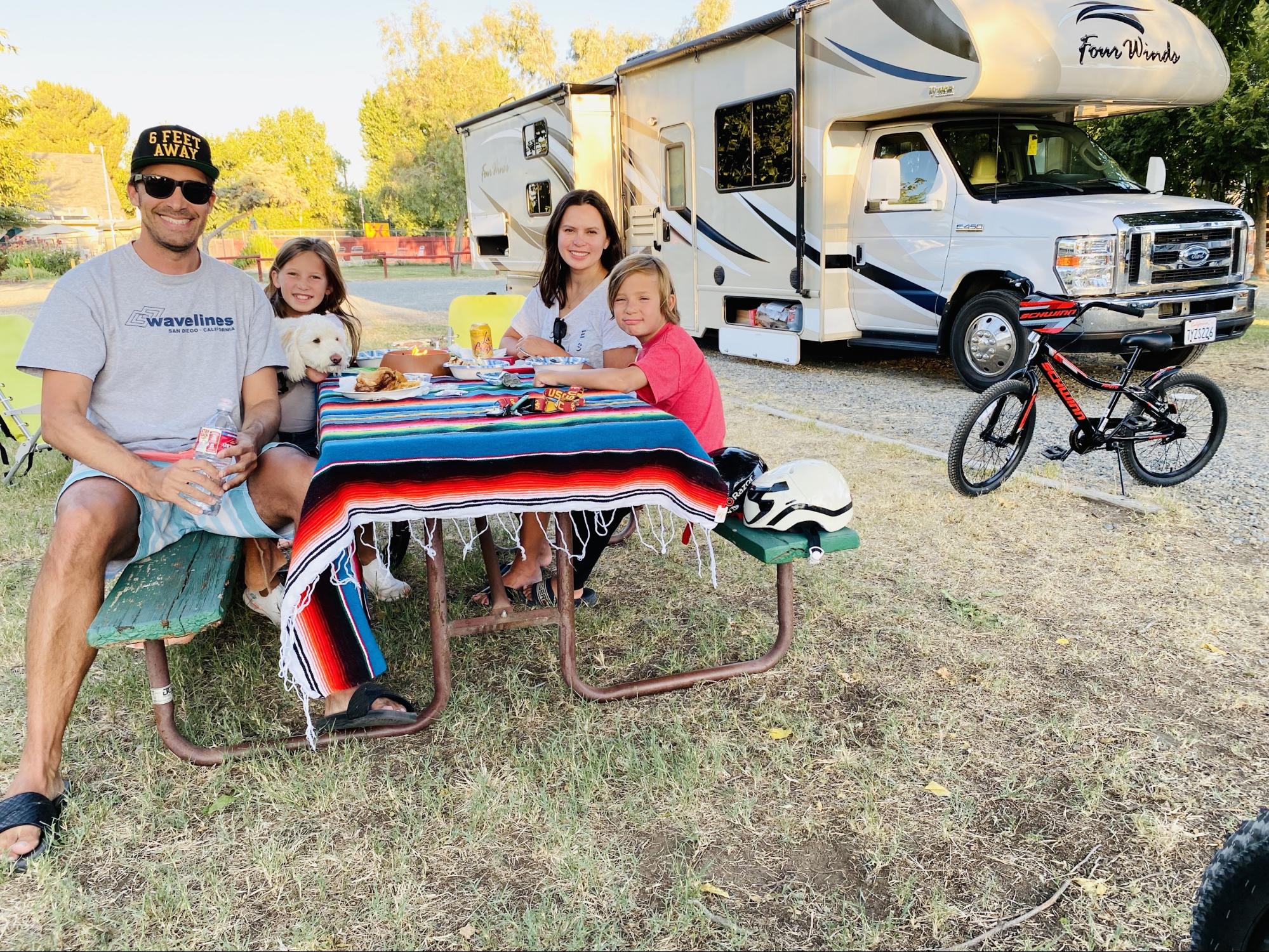 Raoul Martinez and his family sit by a picnic table in front of a Thor Motor Coach Four Winds Class C RV.