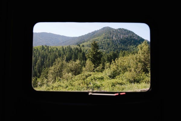 A view from inside an RV looking out the window to see mountains filled with lush, green trees.