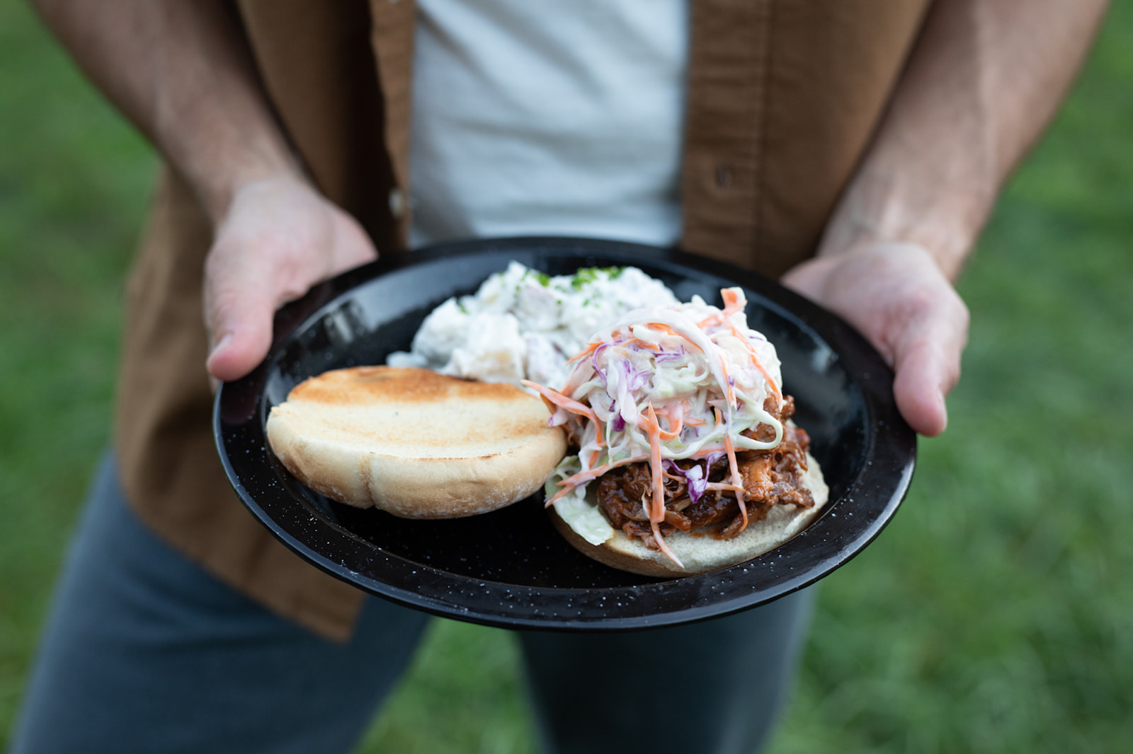 A close up of a barbeque pulled pork sandwich with coleslaw and potato salad.