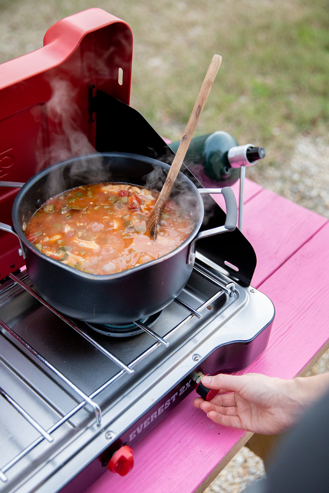 A wooden spoon resting in a pot of sauce on a camp stove.