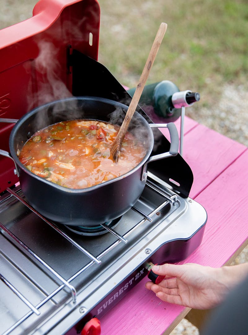 A wooden spoon resting in a pot of sauce on a camp stove.