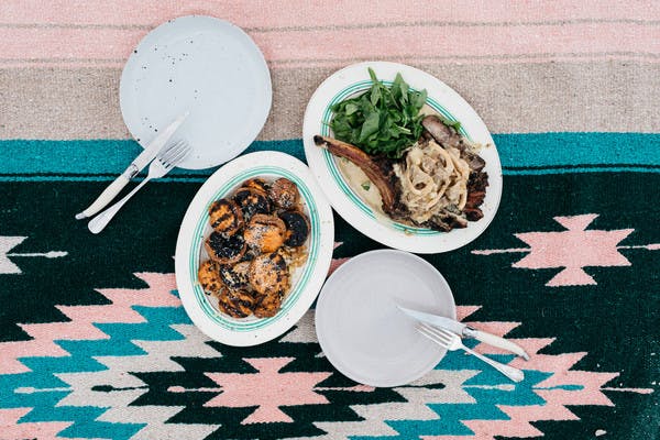 Dishes on a table holding a tomahawk steak topped with onions and cheesy sweet potato rounds.