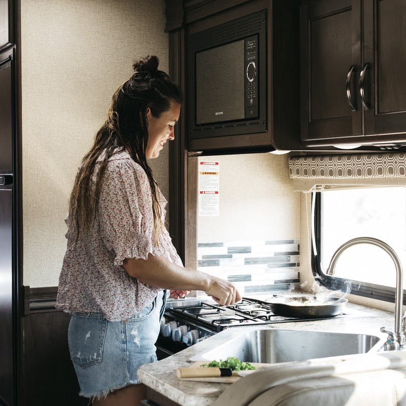 Sarah Glover cooking swiss chard and pesto shakshuka recipe over RV kitchen stove.